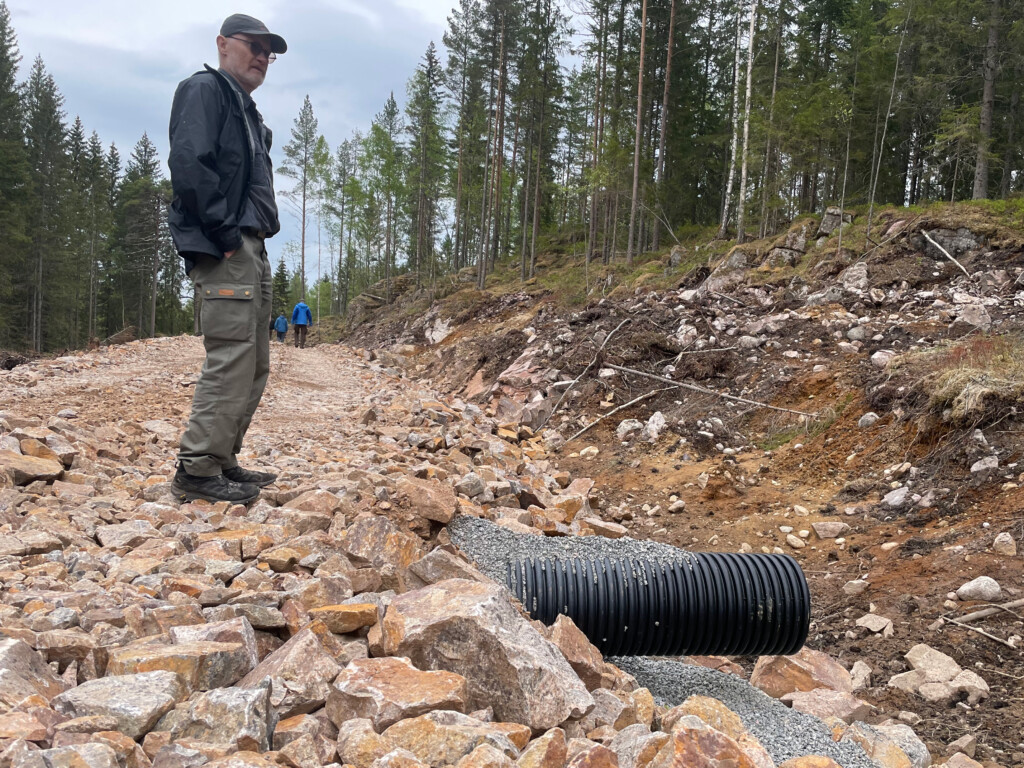 Mann som står på bærelaget på en skogsbilvei. En stikkrenne stikker langt ut på siden. Foto.